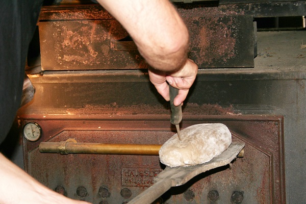 Brot wird in den Holzbackofen geschoben