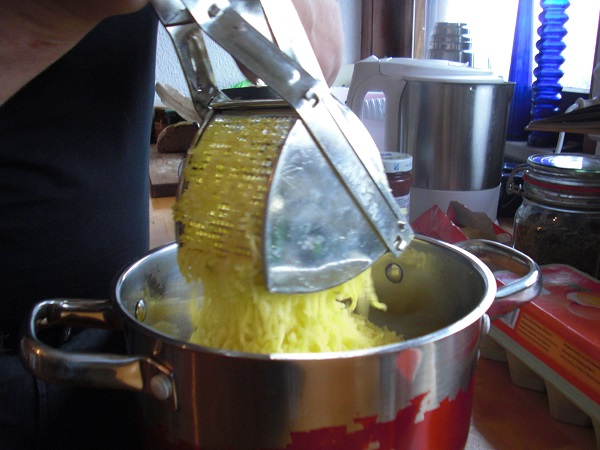 Mit einer Kartoffelpresse die gekochten Kartoffeln zerdrücken