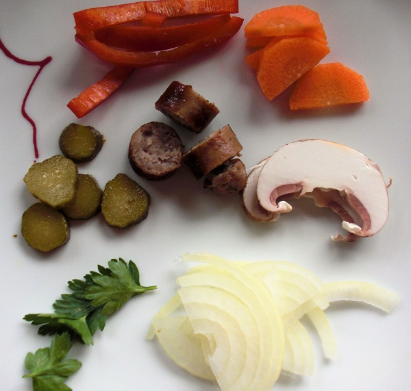 Foto kleingeschnittene Bratwurst Essiggkurke Zwiebeln Karotten auf weißem Teller