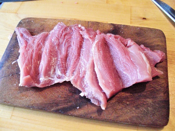 Foto Schweinelende mit Schmetterlingsschnitt zu einer flachen Roulade geschnitten auf Holzbrettchen