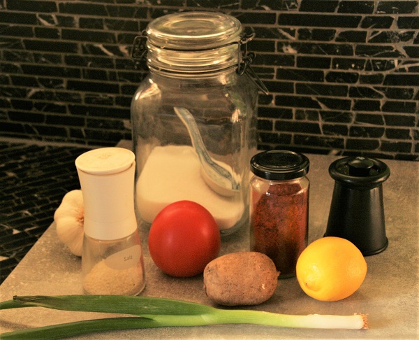 Foto Gewürze für Fischsuppe Zucker im Bügelglas Paprikapulver im Schraubglas Salz Pfeffermühle eine Tomate Kartoffel Zitrone und Frühlingszwiebel auf einer grauen Steinplatte