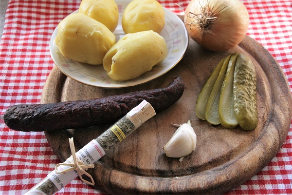 Foto Zutaten für fränkische Bauernpfanne. Zwiebeln, Kartoffeln, Knoblauch, Essiggurken und geräucherte Bratwürste