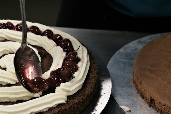 Foto Biskuitboden einer echte Schwarzwälder Kirschtorte wird mit Sahne und Kirschen bedeckt