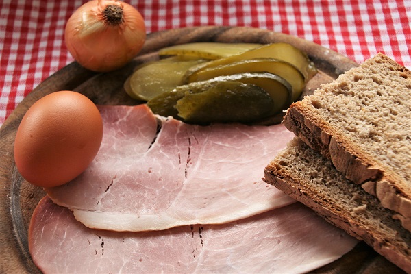 Foto Zutaten für fränkisches Bauernfrühstück Schinken, Essiggurken, Ei und Brot auf Holzteller